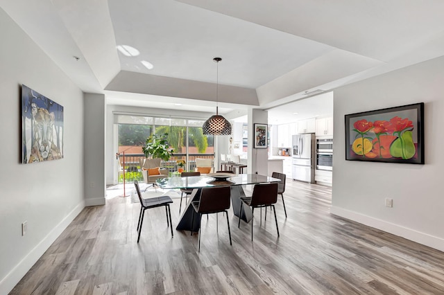 dining area featuring light wood-style flooring, baseboards, and a tray ceiling