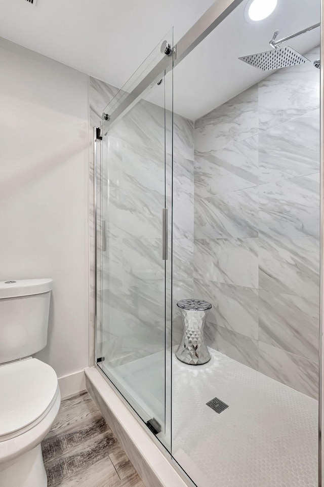 full bath featuring toilet, wood finished floors, baseboards, and a marble finish shower