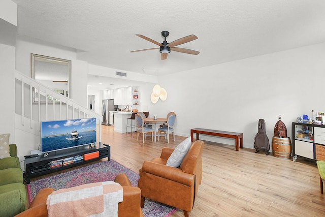 living room with a textured ceiling, light hardwood / wood-style flooring, and ceiling fan