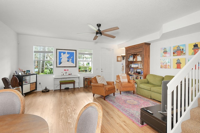 living room with a textured ceiling, light wood-type flooring, and ceiling fan