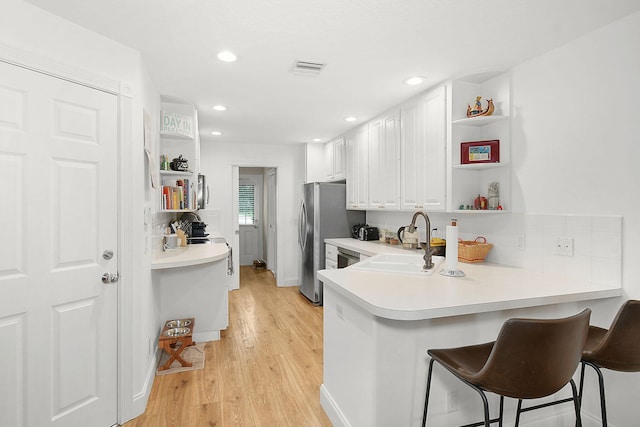 kitchen featuring a breakfast bar, sink, white cabinetry, light hardwood / wood-style floors, and kitchen peninsula