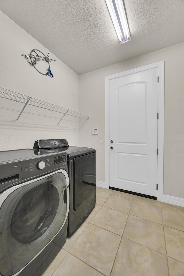 clothes washing area featuring a textured ceiling, light tile patterned flooring, and washer and dryer