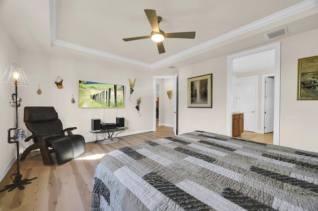 bedroom with ceiling fan, connected bathroom, a tray ceiling, crown molding, and light hardwood / wood-style flooring