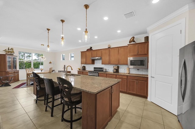 kitchen featuring a center island with sink, appliances with stainless steel finishes, decorative light fixtures, a kitchen breakfast bar, and ornamental molding