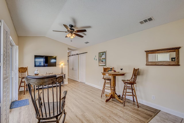 sitting room featuring a textured ceiling, a barn door, vaulted ceiling, and ceiling fan