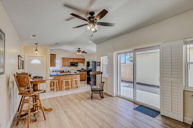 kitchen with a breakfast bar, black appliances, vaulted ceiling, light wood-type flooring, and kitchen peninsula