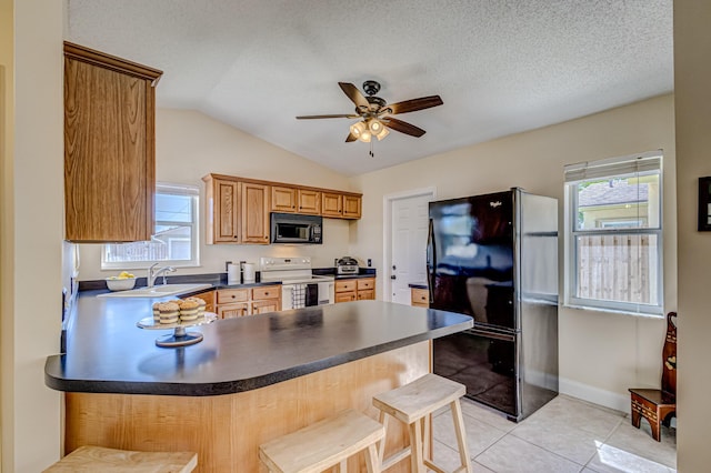 kitchen with black appliances, vaulted ceiling, light tile patterned floors, a textured ceiling, and a breakfast bar area