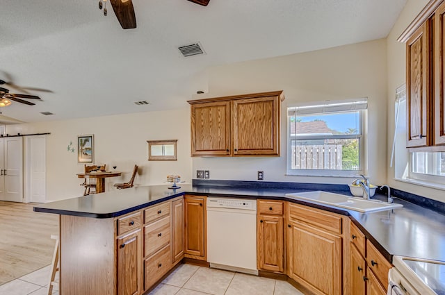 kitchen featuring dishwasher, sink, kitchen peninsula, light tile patterned floors, and range