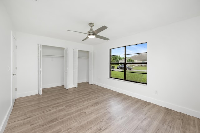 unfurnished bedroom featuring multiple closets, ceiling fan, and light hardwood / wood-style flooring