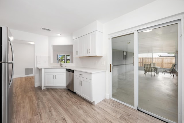 kitchen featuring sink, tasteful backsplash, appliances with stainless steel finishes, white cabinets, and light wood-type flooring