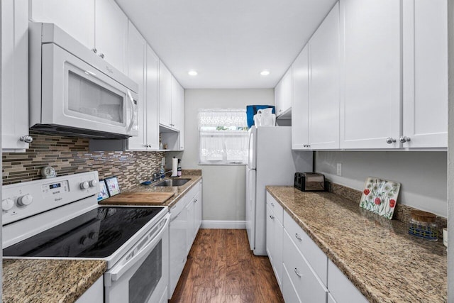 kitchen with white appliances, white cabinets, sink, dark hardwood / wood-style floors, and dark stone countertops