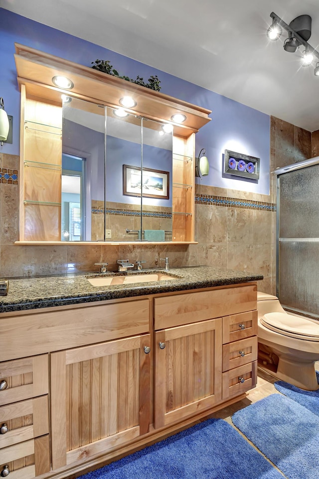 bathroom with tile walls, vanity, a shower with door, and toilet