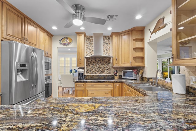 kitchen with appliances with stainless steel finishes, tasteful backsplash, dark stone counters, sink, and wall chimney range hood