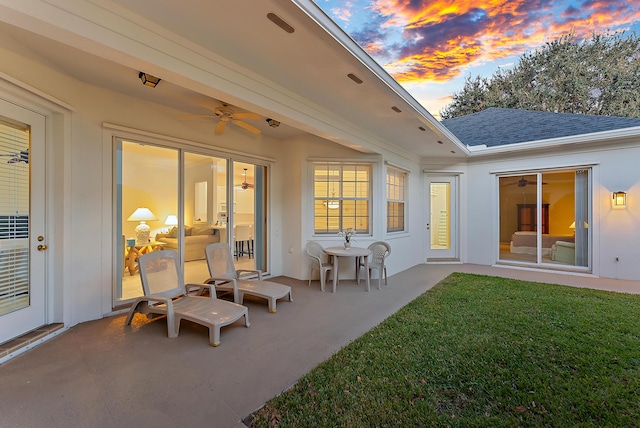 back house at dusk featuring a lawn, ceiling fan, and a patio area