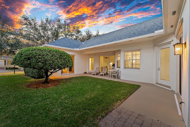 back house at dusk featuring a lawn and a patio