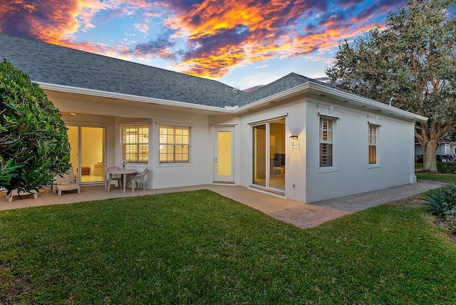 back house at dusk featuring a patio area and a lawn