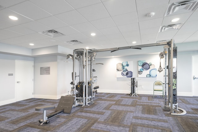 exercise room with a paneled ceiling and dark carpet