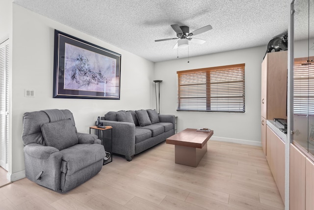 living room featuring ceiling fan, light hardwood / wood-style flooring, and a textured ceiling