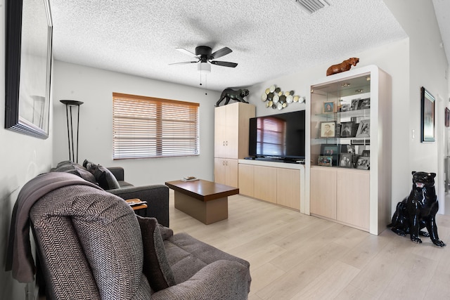 living room with ceiling fan, light wood-type flooring, and a textured ceiling