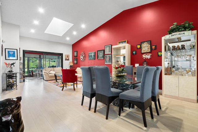 dining area featuring light wood-type flooring, a skylight, and high vaulted ceiling