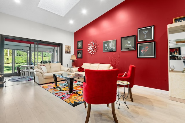 living room featuring light hardwood / wood-style floors, high vaulted ceiling, and a skylight