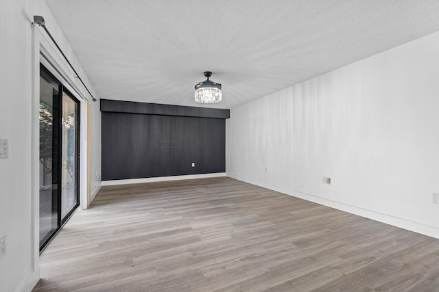 spare room with light hardwood / wood-style flooring, a textured ceiling, and an inviting chandelier