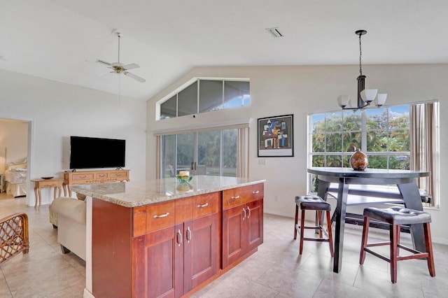 kitchen with light stone countertops, a center island, decorative light fixtures, vaulted ceiling, and ceiling fan with notable chandelier