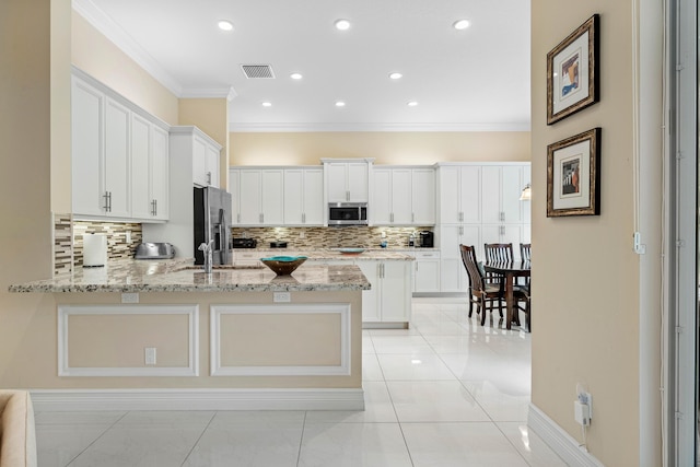 kitchen with kitchen peninsula, appliances with stainless steel finishes, white cabinets, and light stone countertops