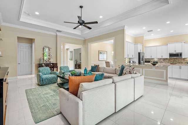 living room with ceiling fan, light tile patterned floors, a tray ceiling, and ornamental molding