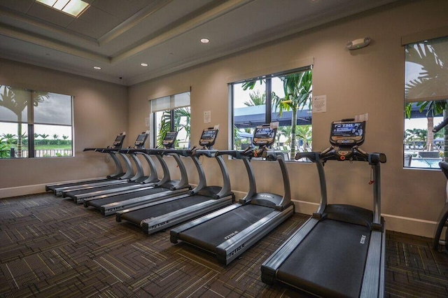 gym featuring a wealth of natural light, ornamental molding, dark carpet, and a tray ceiling