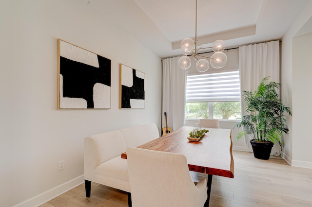 dining area with a tray ceiling, light hardwood / wood-style flooring, and a notable chandelier