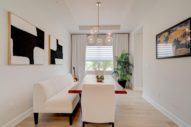 dining space with a tray ceiling, an inviting chandelier, and light wood-type flooring