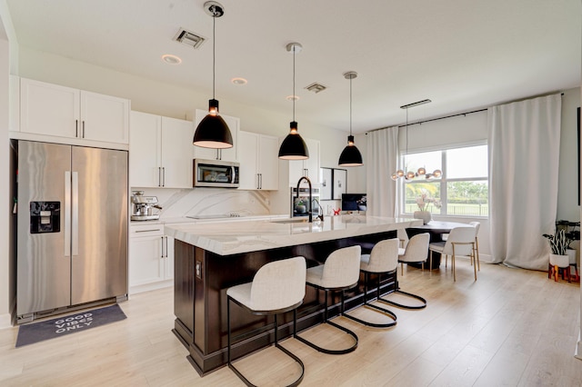 kitchen featuring stainless steel appliances, light stone counters, pendant lighting, a center island with sink, and white cabinets