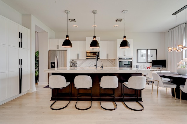 kitchen with a center island with sink, pendant lighting, white cabinetry, and stainless steel appliances