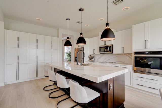 kitchen with a kitchen island with sink, sink, decorative backsplash, appliances with stainless steel finishes, and white cabinetry