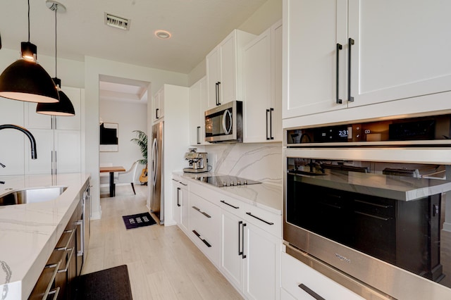 kitchen featuring appliances with stainless steel finishes, light stone counters, sink, decorative light fixtures, and white cabinets