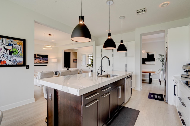 kitchen with dark brown cabinetry, sink, hanging light fixtures, stainless steel dishwasher, and a kitchen island with sink