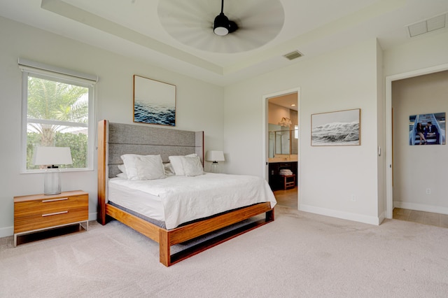 bedroom featuring ceiling fan, a raised ceiling, light carpet, and ensuite bath