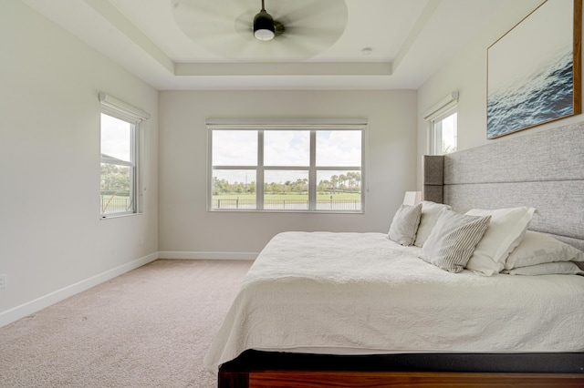 bedroom with a raised ceiling, multiple windows, and ceiling fan