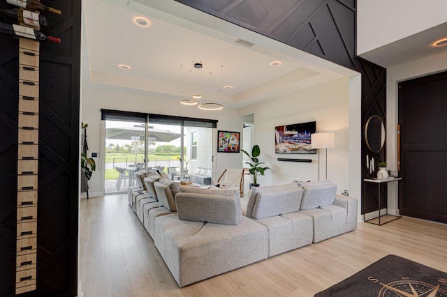 living room with a raised ceiling and light wood-type flooring