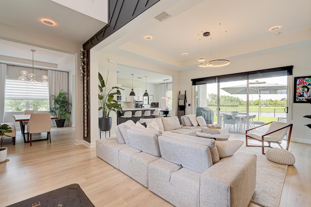 living room with a raised ceiling, light hardwood / wood-style flooring, and a chandelier