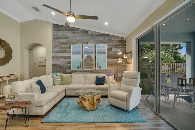 living room featuring lofted ceiling, light wood-type flooring, wood walls, and ornamental molding