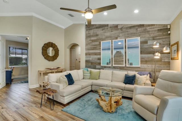 living room with light hardwood / wood-style floors, ornamental molding, wood walls, vaulted ceiling, and ceiling fan