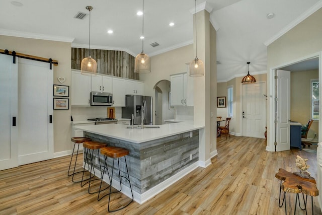 kitchen with a barn door, a breakfast bar, hanging light fixtures, stainless steel appliances, and white cabinets