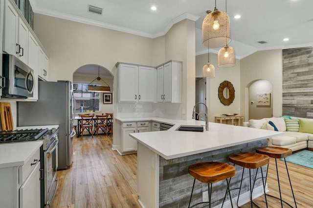 kitchen featuring a kitchen bar, sink, light hardwood / wood-style flooring, hanging light fixtures, and appliances with stainless steel finishes