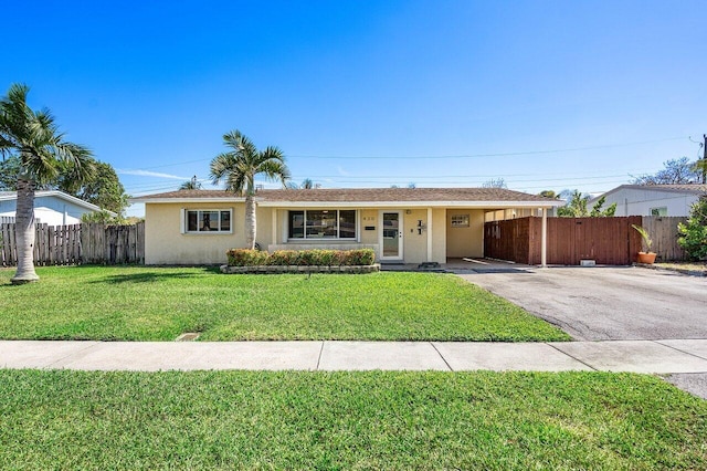 ranch-style house featuring driveway, a front yard, stucco siding, fence, and a carport