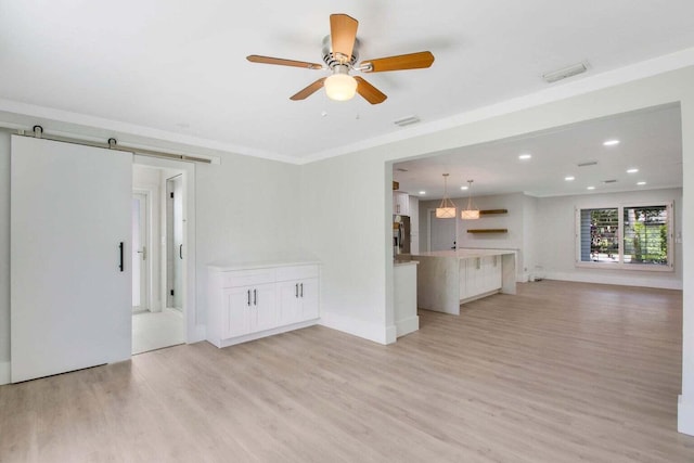 unfurnished living room with ceiling fan, a barn door, light hardwood / wood-style floors, and crown molding