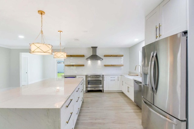 kitchen featuring tasteful backsplash, appliances with stainless steel finishes, white cabinets, pendant lighting, and wall chimney range hood