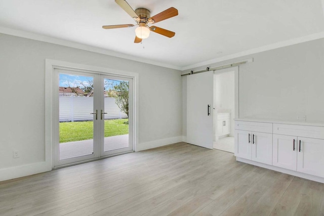 spare room featuring ceiling fan, ornamental molding, a barn door, and light wood-type flooring