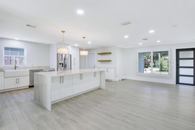 kitchen with a kitchen island, white cabinetry, sink, hanging light fixtures, and stainless steel appliances